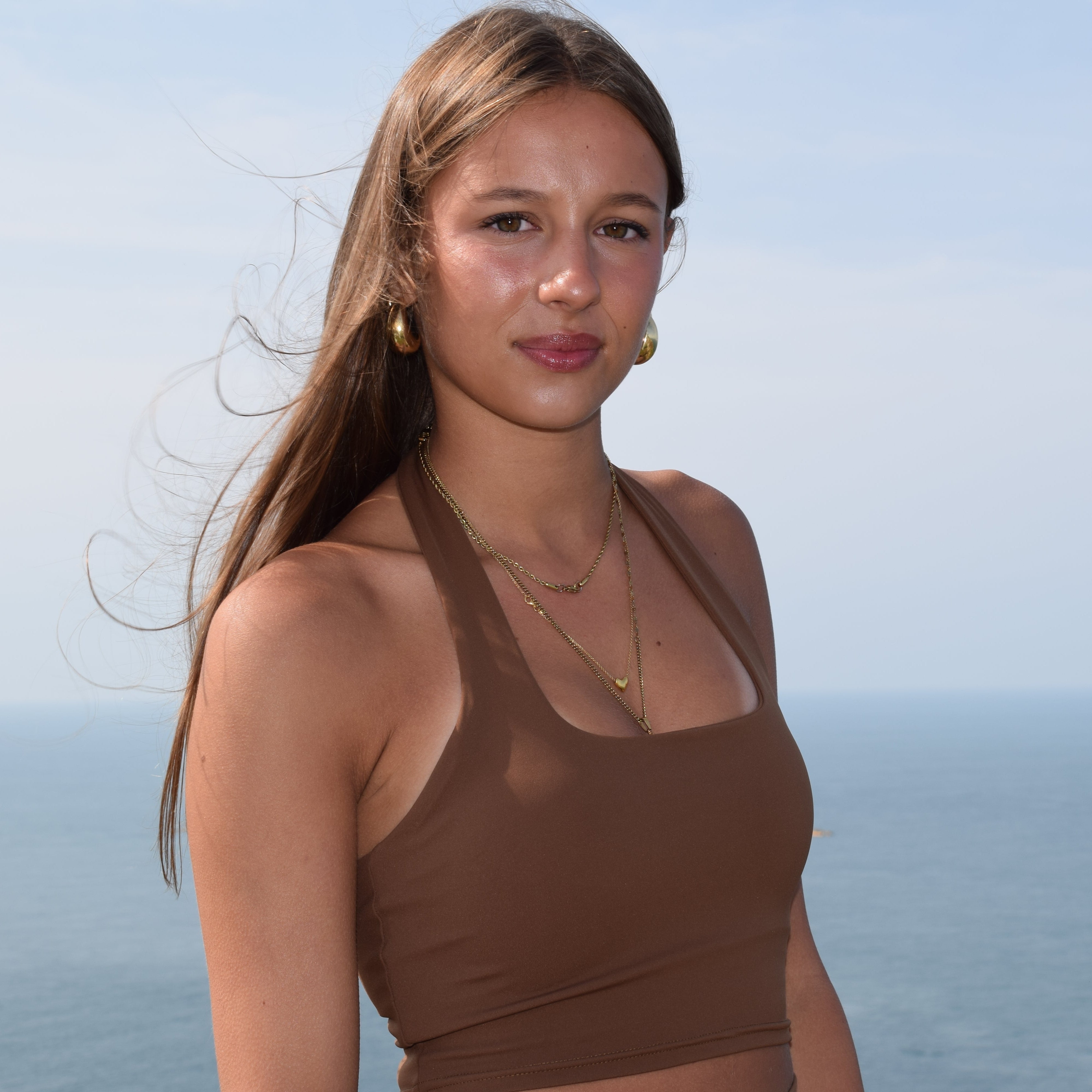 Woman in a brown top standing against a clear blue sky
