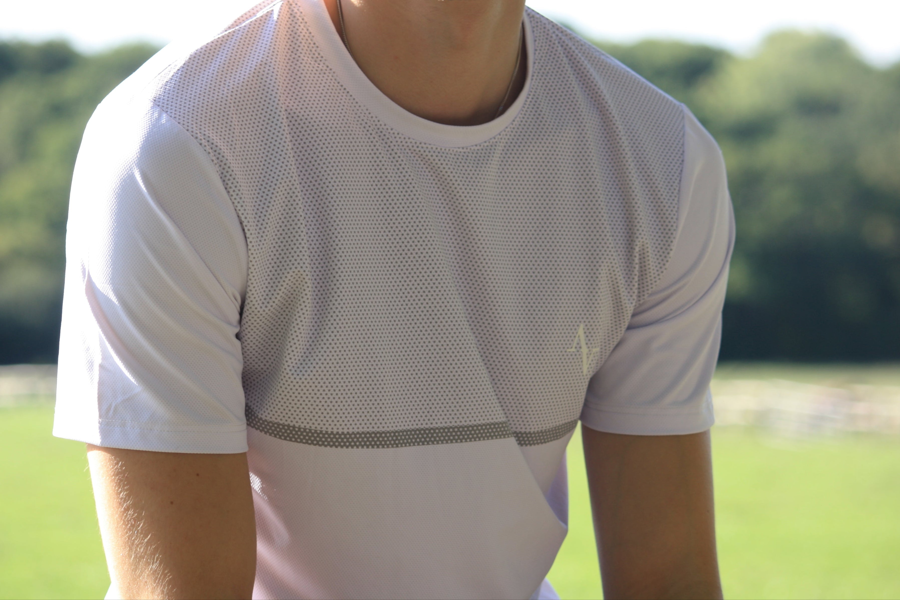Person wearing a white athletic shirt outdoors with greenery in the background